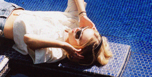 girl sitting on a diving board above a pool with sunglasses and headphones on as she listens to music