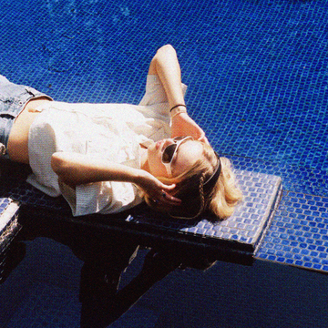 girl sitting on a diving board above a pool with sunglasses and headphones on as she listens to music