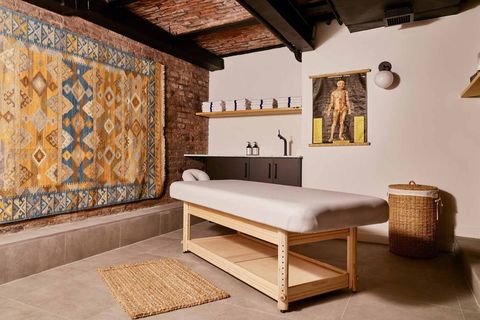 a massage table in a brick walled room with an ornate woven tapestry