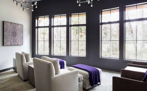 two gray chairs draped in purple blankets facing a wall of windows with views to a forest