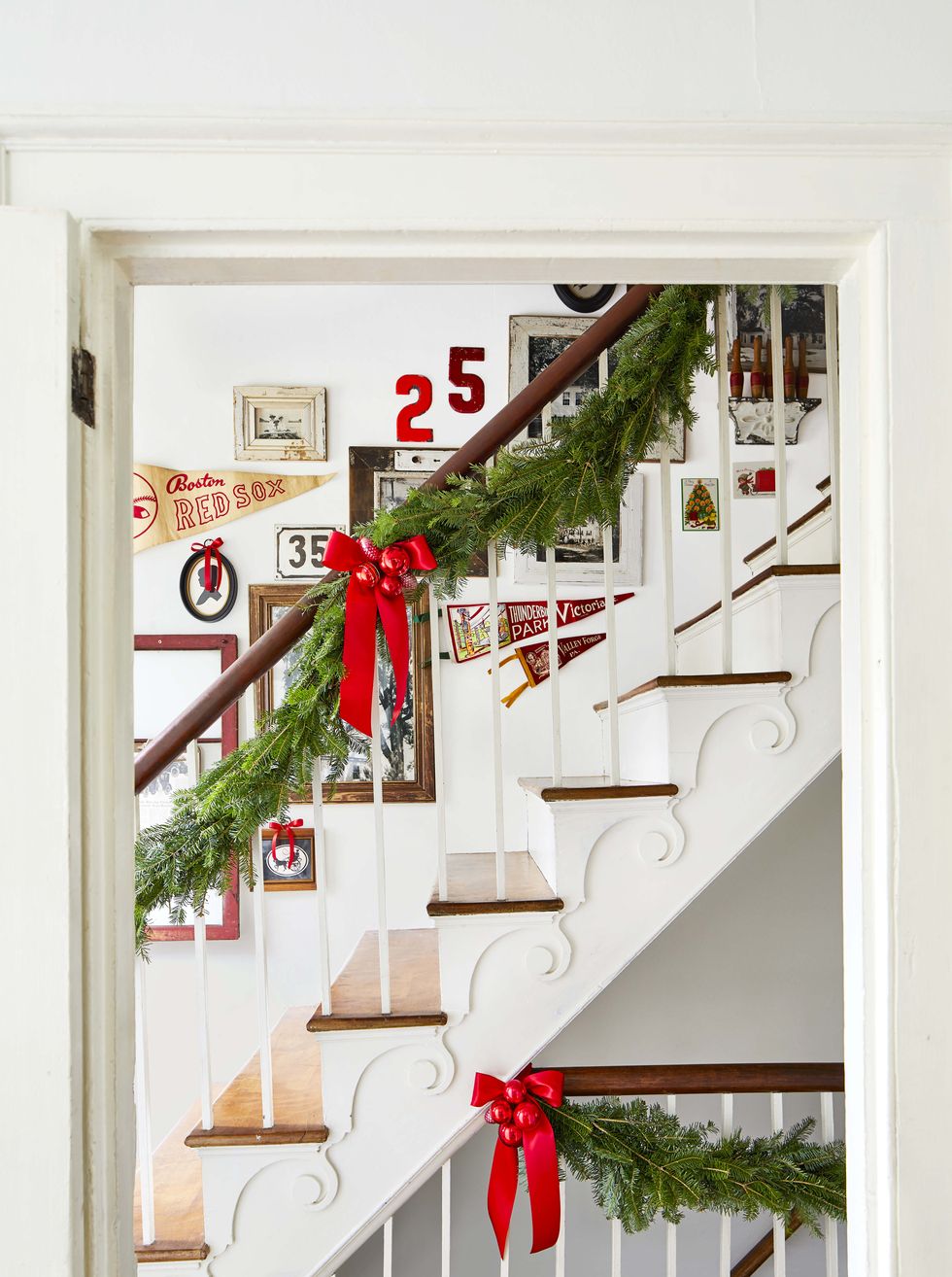 red bows with red christmas balls in the middle decorate a staircase with greenery