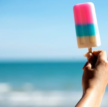 best summer instagram captions hand holding a pink blue and white popsicle by the beach