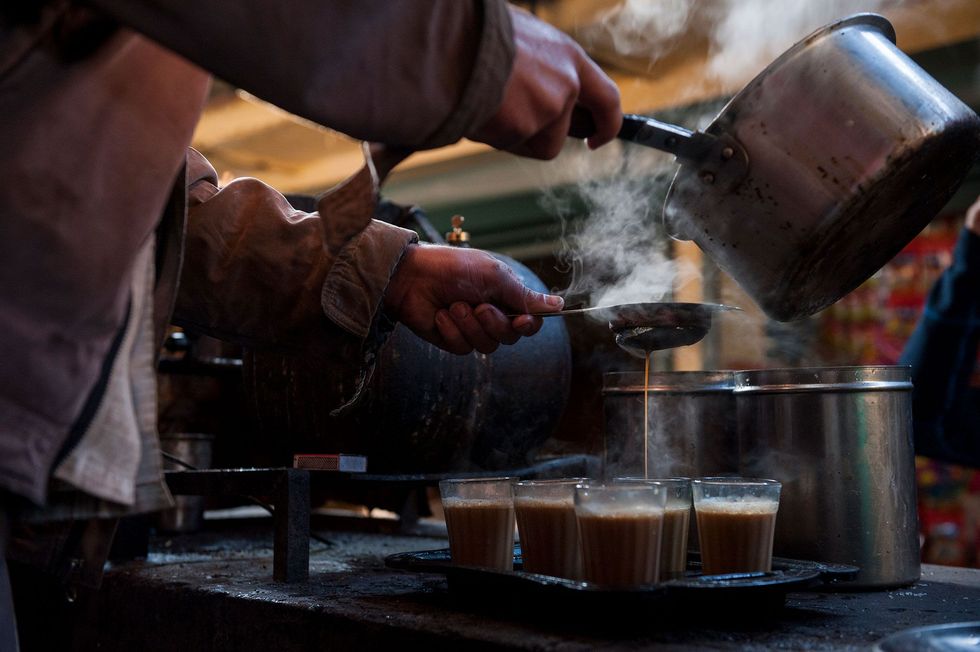 Een man giet heet water door een zeefje om masala chai te bereiden