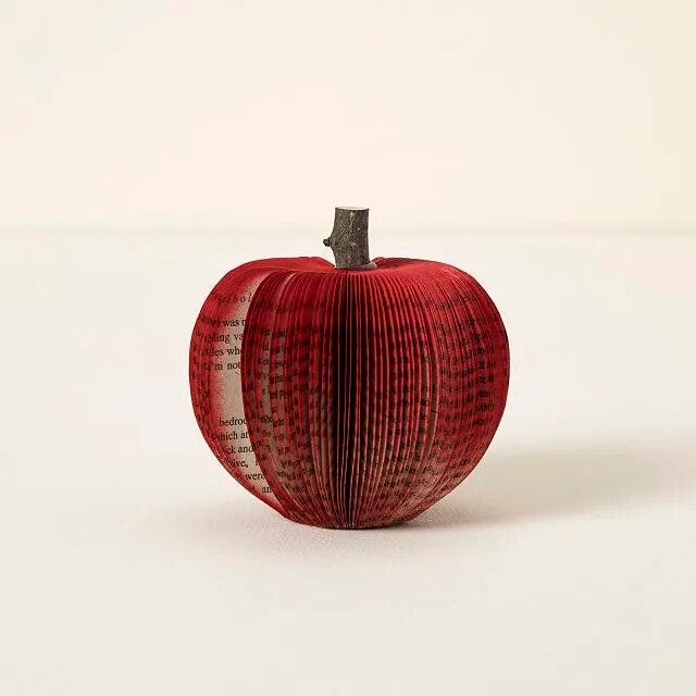 a red paper apple made from book pages with a wooden stem from a tree