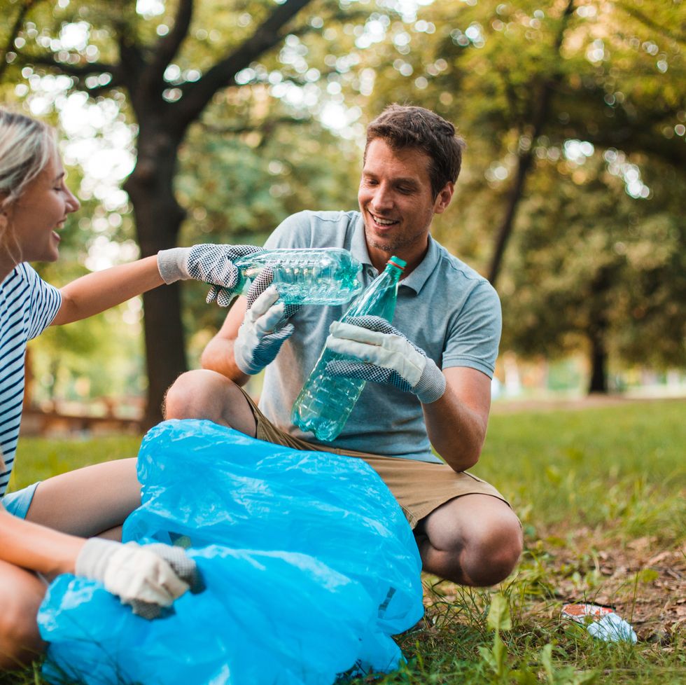 diligent young couple recycling bottles using plastic bags and gloves and smiling