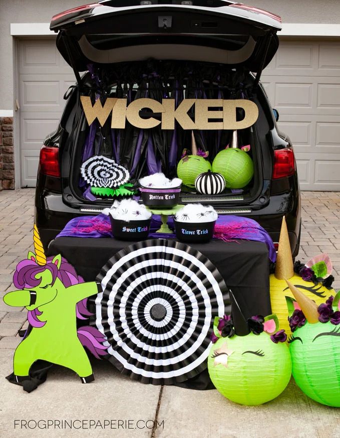 vehicle tailgate open with wicked in gold letters spelled out on a banner across opening, unicorn heads made out of green paper lanterns a green cartoon unicorn standup sitting in front of the tailgate and sitting on the tailgate are black plastic cauldrons labeled clever trick sweet trick and rotten trick