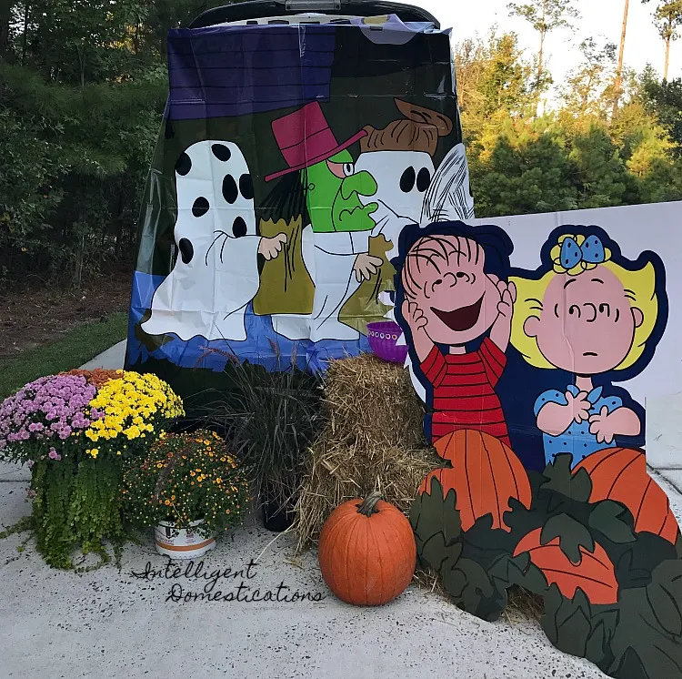 back end of a vehicle open with lucy and linus and other peanuts halloween cut outs sitting in it and around it with hay bales and mums and a pumpkin