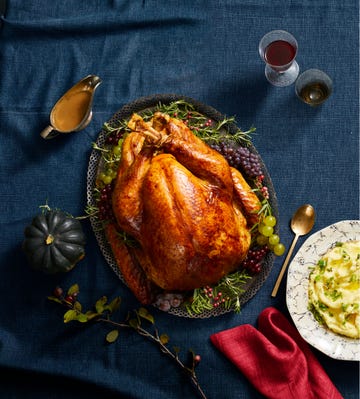 a whole golden turkey on a serving platter with red and green grapes on the side