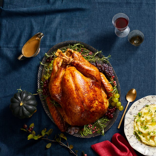 a whole golden turkey on a serving platter with red and green grapes on the side