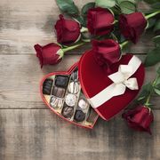 valentines day box of chocolates and red roses on a wood background