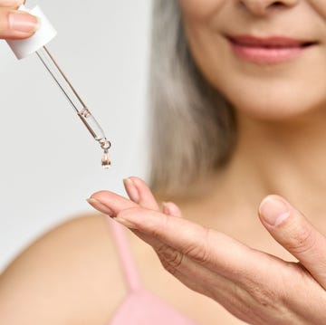 close up of woman putting serum onto hand from pipette