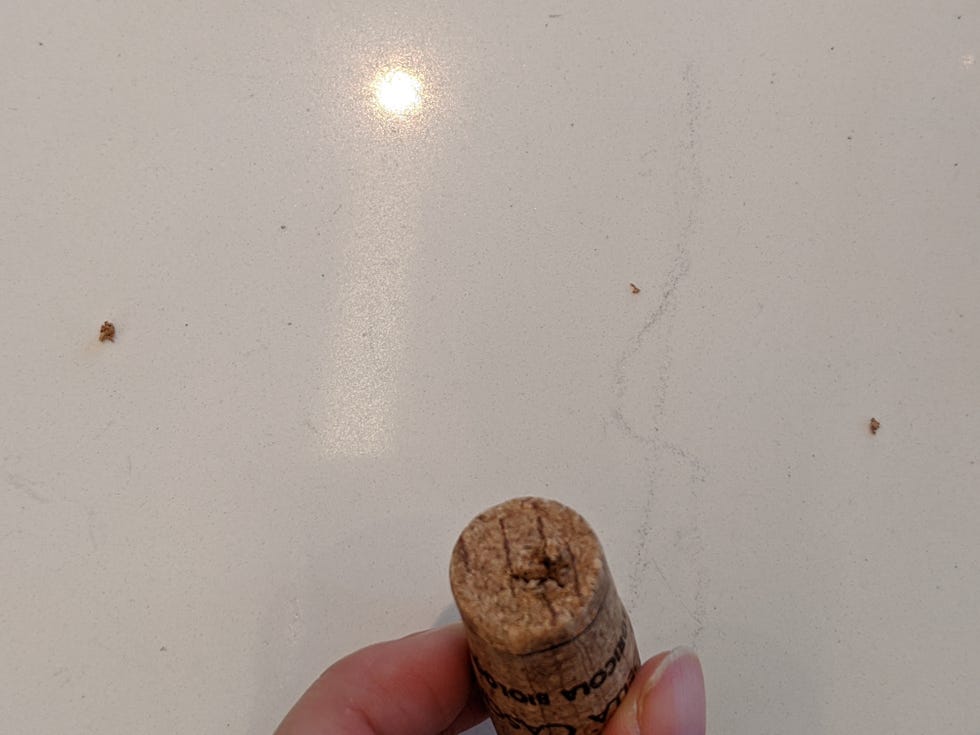closeup of a wine cork held in hand with bits of cork on countertop