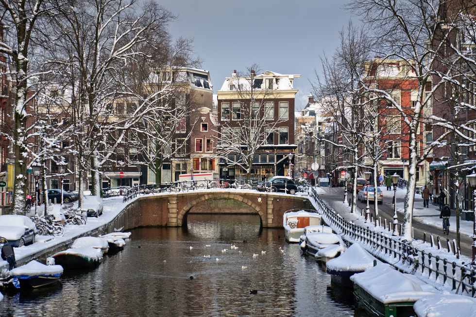 bridge, boats and building cover by snow fall in amsterdam, netherlands