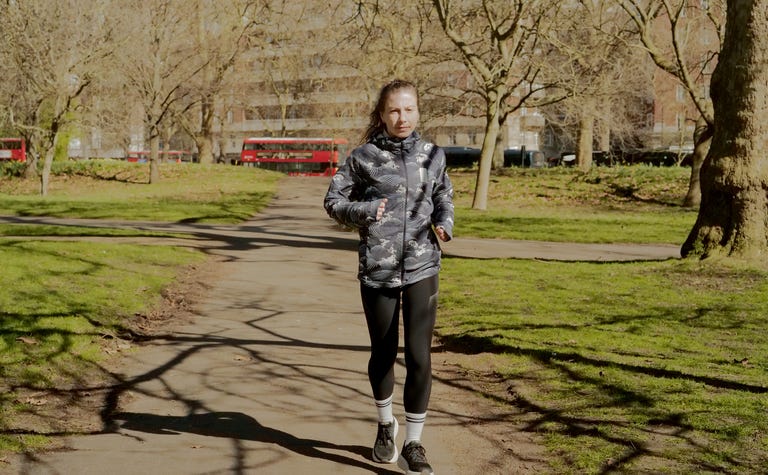 a woman jogging through a park wearing black leggings and a waterproof jacket