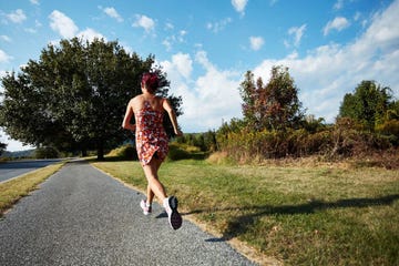 woman running on a path surrounded by trees and grass under a blue sky