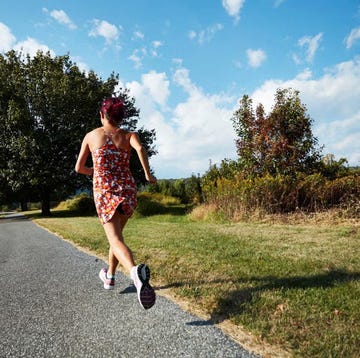 woman running on a path surrounded by trees and grass under a blue sky woman running on a path surrounded by trees and grass under a blue sky