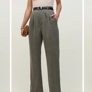 a model wears the reformation mason pant in front of a plain backdrop with a belt and sandals in a roundup of the best work pants for women 2022