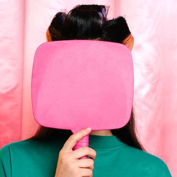 woman with curlers covering face with pink mirror