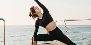 best yoga retreats: Young brunette woman in a black jumpsuit practicing yoga on the beach at sunrise. Concept of wellness and healthy lifestyle.
