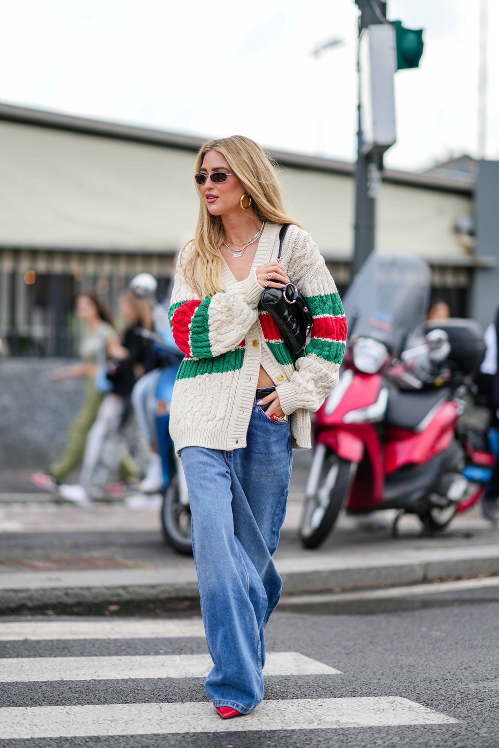 milan, italy september 22 emili sindlev wears sunglasses, earrings, a necklace, a green red and white striped logo wool knit cardigan, a black leather bag, blue denim wide leg jeans pants, red pointed shoes, outside gucci, during the milan fashion week womenswear springsummer 2024 on september 22, 2023 in milan, italy photo by edward berthelotgetty images