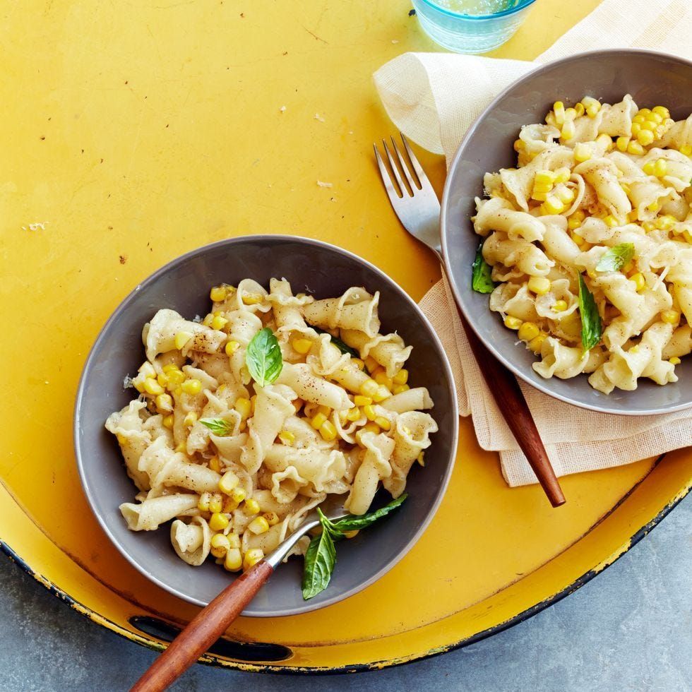 two bowls of campanelle pasta with brown butter and corn in grey dishes on yellow background