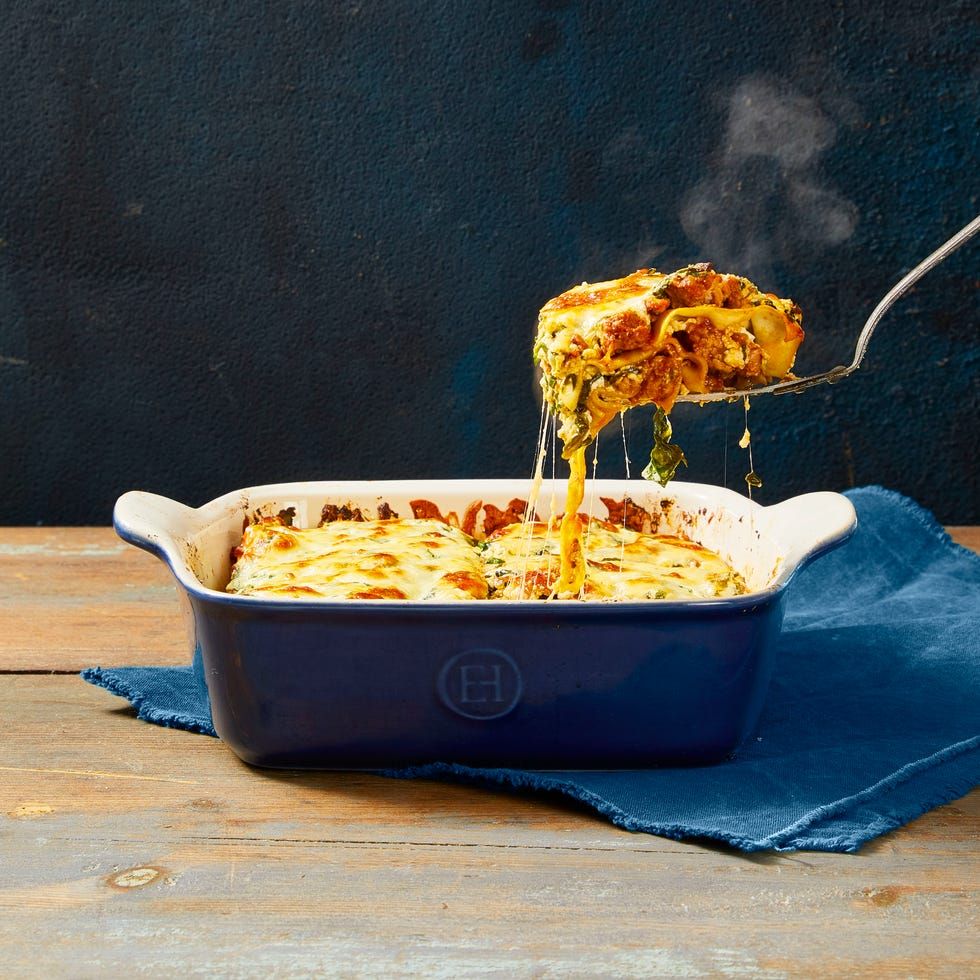 spatula lifting a slice from a lasagna with meat sauce in a blue casserole dish