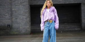 copenhagen, denmark february 01 emili sindlev wears blue earrings, a pale purple large fluffy fur jacket, a white t shirt, a purple shiny leather quilted timeless handbag from chanel, a gold shiny leather flower buckle belt, blue with white painted logo and polka dots print pattern denim wide legs pants from chanel, white shiny leather pointed pumps heels shoes , outside a roege hove, during the copenhagen fashion week autumnwinter 2023 on february 01, 2023 in copenhagen, denmark photo by edward berthelotgetty images