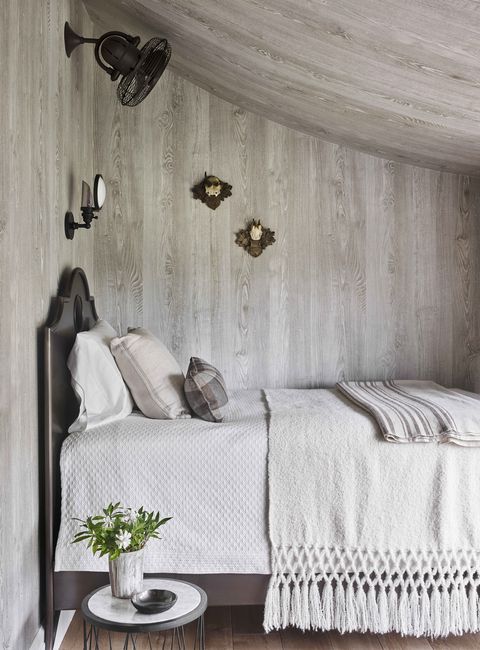 a bed in neutral linens tucked under the eaves and the wallcovering is faux bois