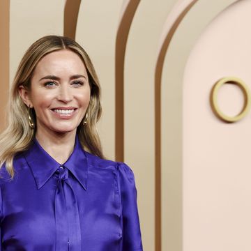 emily blunt smiles at the camera, she wears an all purple outfit