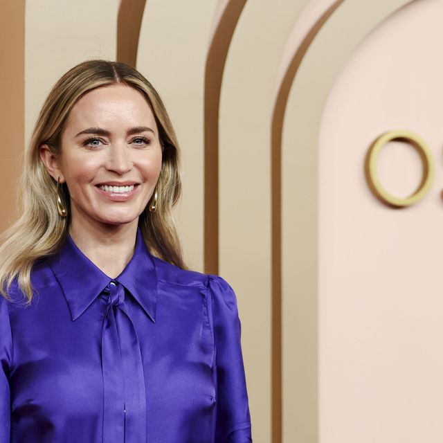 emily blunt smiles at the camera, she wears an all purple outfit