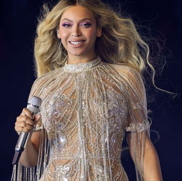 beyonce smiles at the camera, she holds a microphone in one hand and wears a beaded dress with short sleeves and beaded fringe