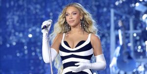 beyonce holding a standing microphone with her right hand and performing at a concert wearing a black and white striped dress