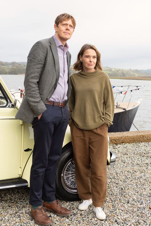 beyond paradise characters humphrey and martha stand in front of a vintage car by the seafront