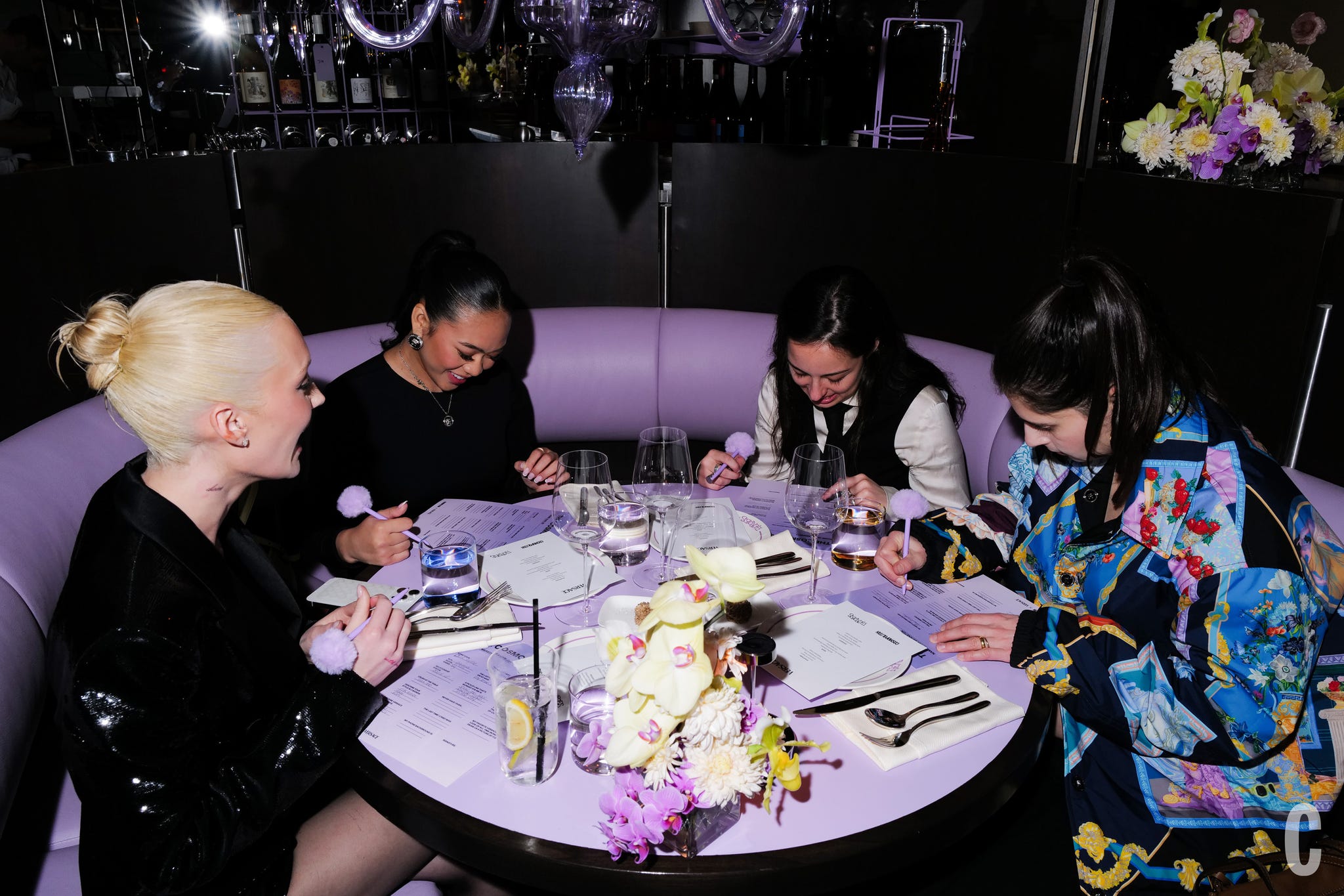 a group of people sitting around a round table and engaged in writing or recording