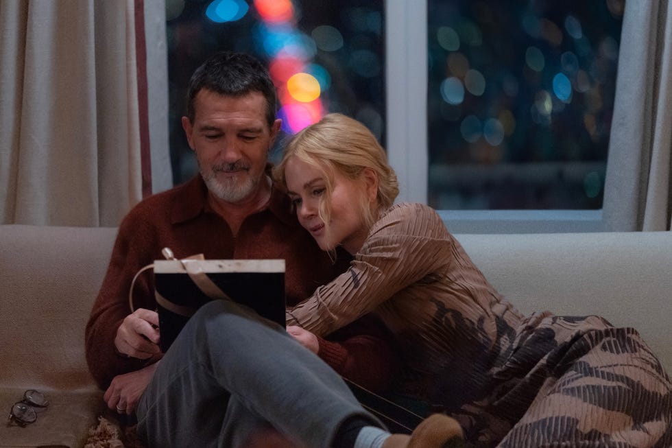 two people sitting close together on a couch one reading from a book