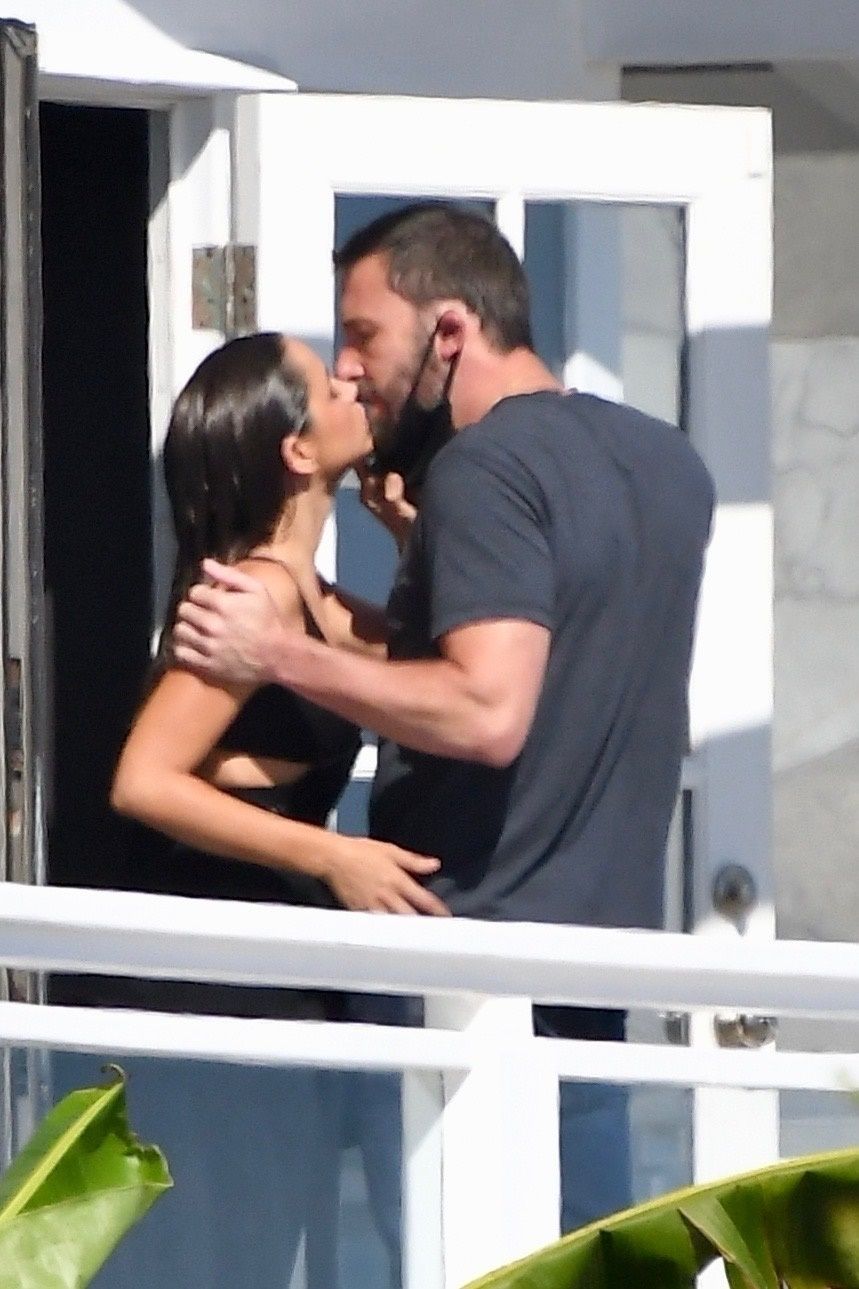 ben pulls down his face mask to kiss ana on a balcony