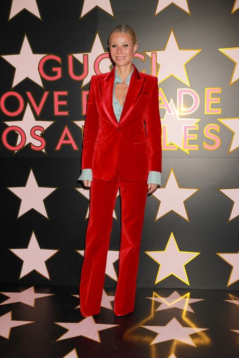 gwyneth poses for a photo in a red velvet suit and blue button down on a black and pink star back drop