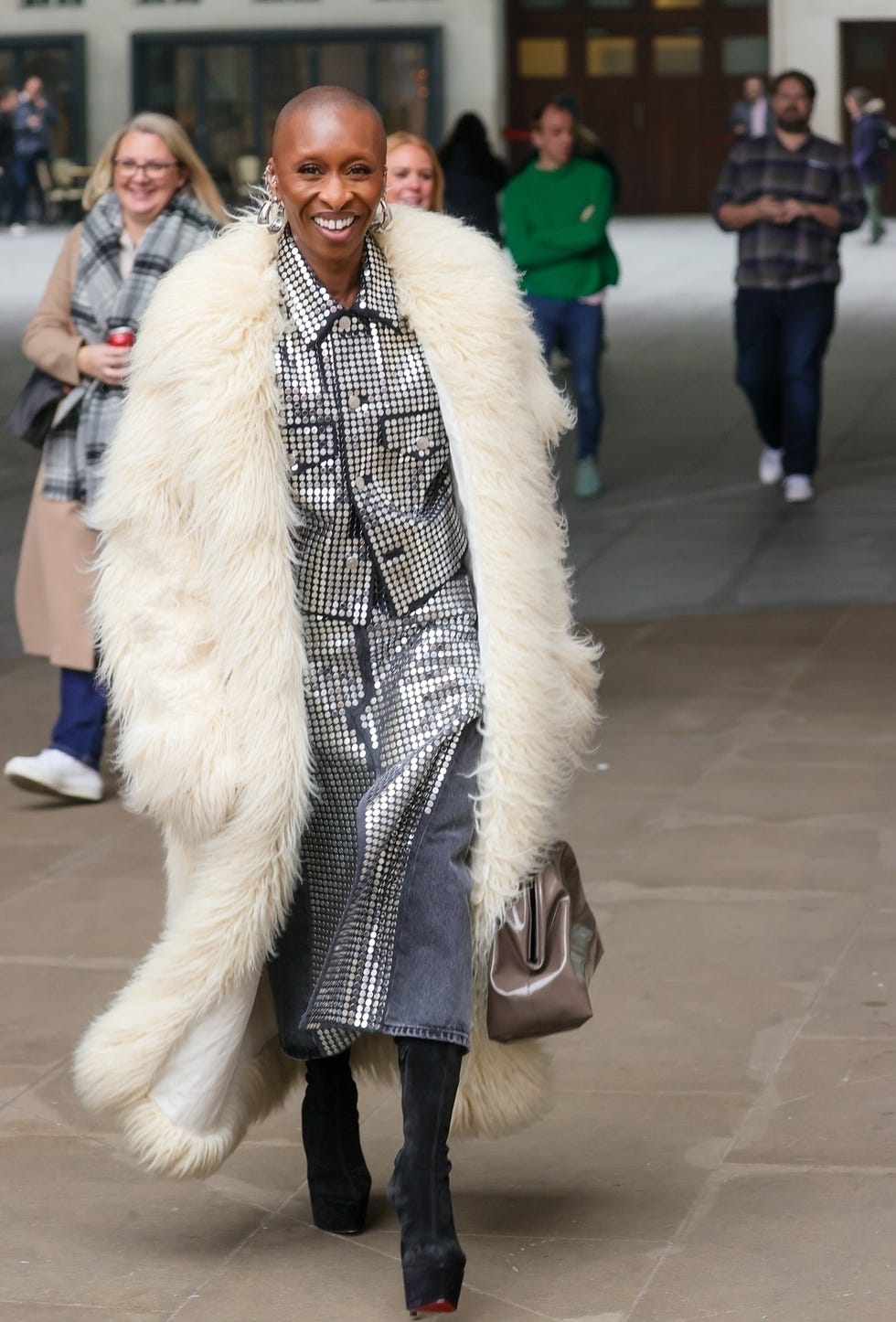 fashionable individual wearing a fur coat and a sequined outfit in a public space