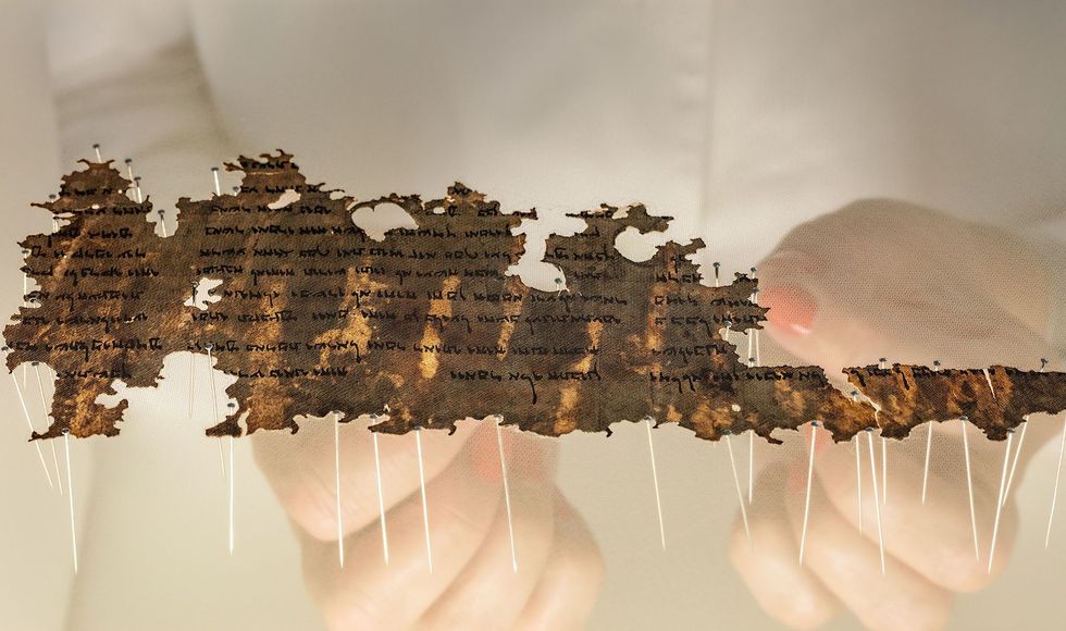 Een conservator van de Isralische Oudheidkundige Dienst prepareert een stukje van de Dode Zeerollen zodat het kan worden gexposeerd De snipper papyrus hier op zn kop wordt tussen twee lagen gaas gelegd die worden afgespeld om daarna te worden vastgenaaid