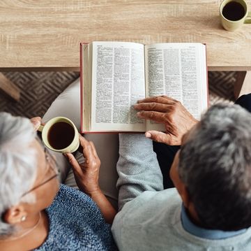 high angle shot of a relaxed elderly couple reading from the bible while drinking coffee at home during the day