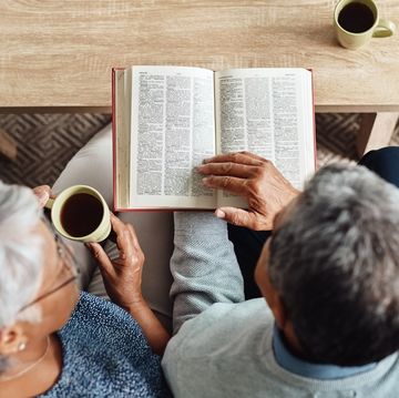 high angle shot of a relaxed elderly couple reading from the bible while drinking coffee at home during the day
