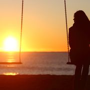 bible verses about grief  silhouette of a woman sitting on a swing looking out at a beach sunset
