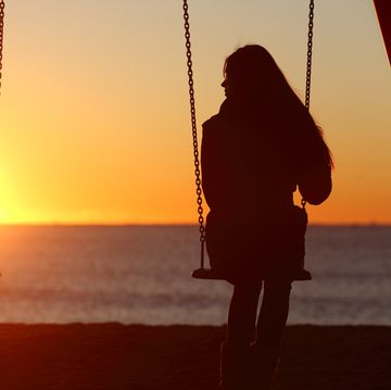 bible verses about grief  silhouette of a woman sitting on a swing looking out at a beach sunset