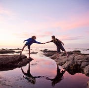 bible verses helping others two people reaching across rocks and water to touch hands with a pink cloud sunset