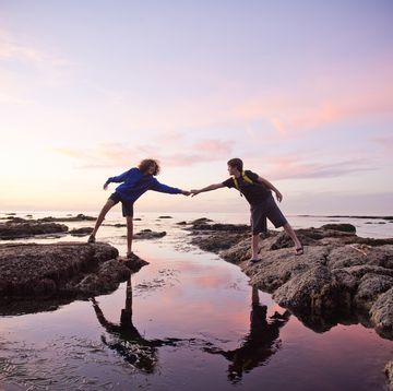 bible verses helping others two people reaching across rocks and water to touch hands with a pink cloud sunset