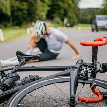 injured cyclist sitting in pain on the road next to the racing bicycle
