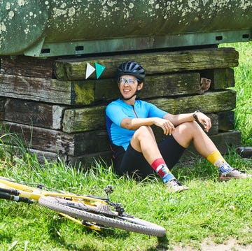 A cyclist resting beside a wooden structure with a bike on the grass A cyclist resting beside a wooden structure with a bike on the grass