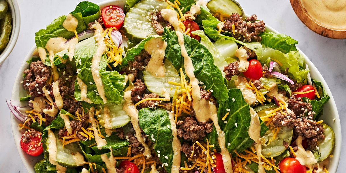 romaine salad topped with ground beef, shredded cheese, sliced baby tomatoes, sliced red onion, sesame seeds, pickles, and mac sauce