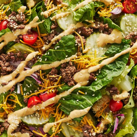 romaine lettuce topped with ground beef, pickles, shredded cheese, cherry tomatoes, red onions, sesame seeds, and a drizzle of mac sauce