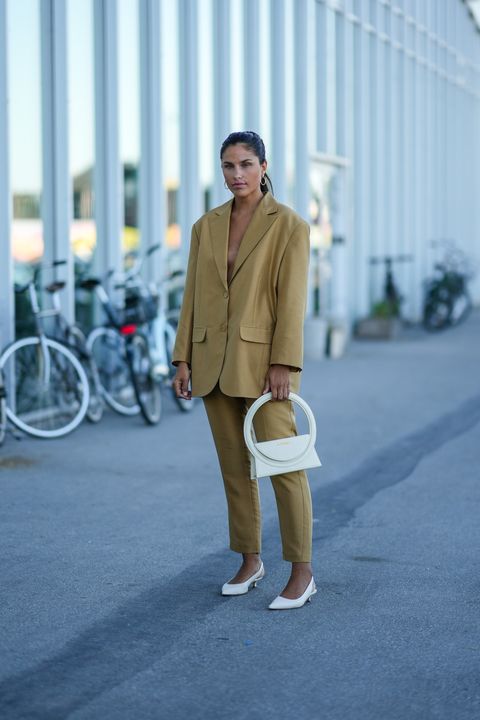 COPENHAGEN, DENMARK AUGUST 11 The guest wears gold earrings, a brown jacket, matching brown pants, a white matte leather Montaigne bag from Jacquemus, white shiny leather heels, outside Montaigne at Copenhagen Fashion Week Spring Winter 2023, August 11, 2018.  2022 in Copenhagen, Denmark Photo by Edward Bertheloghetti Images